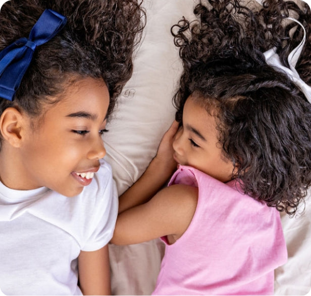 two sisters looking at each other and smiling while laying down 